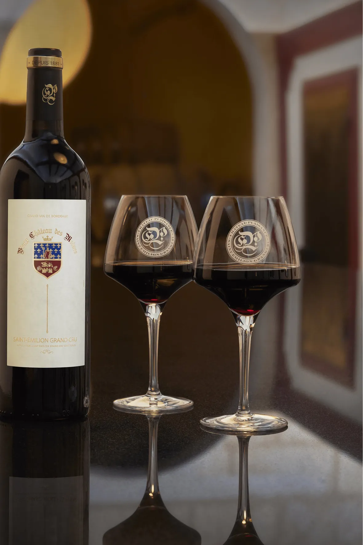 A photograph of a bottle of Vieux Chateau des Moines Saint-Émilion Grand Cru red wine with two glasses by Château Plaisance.