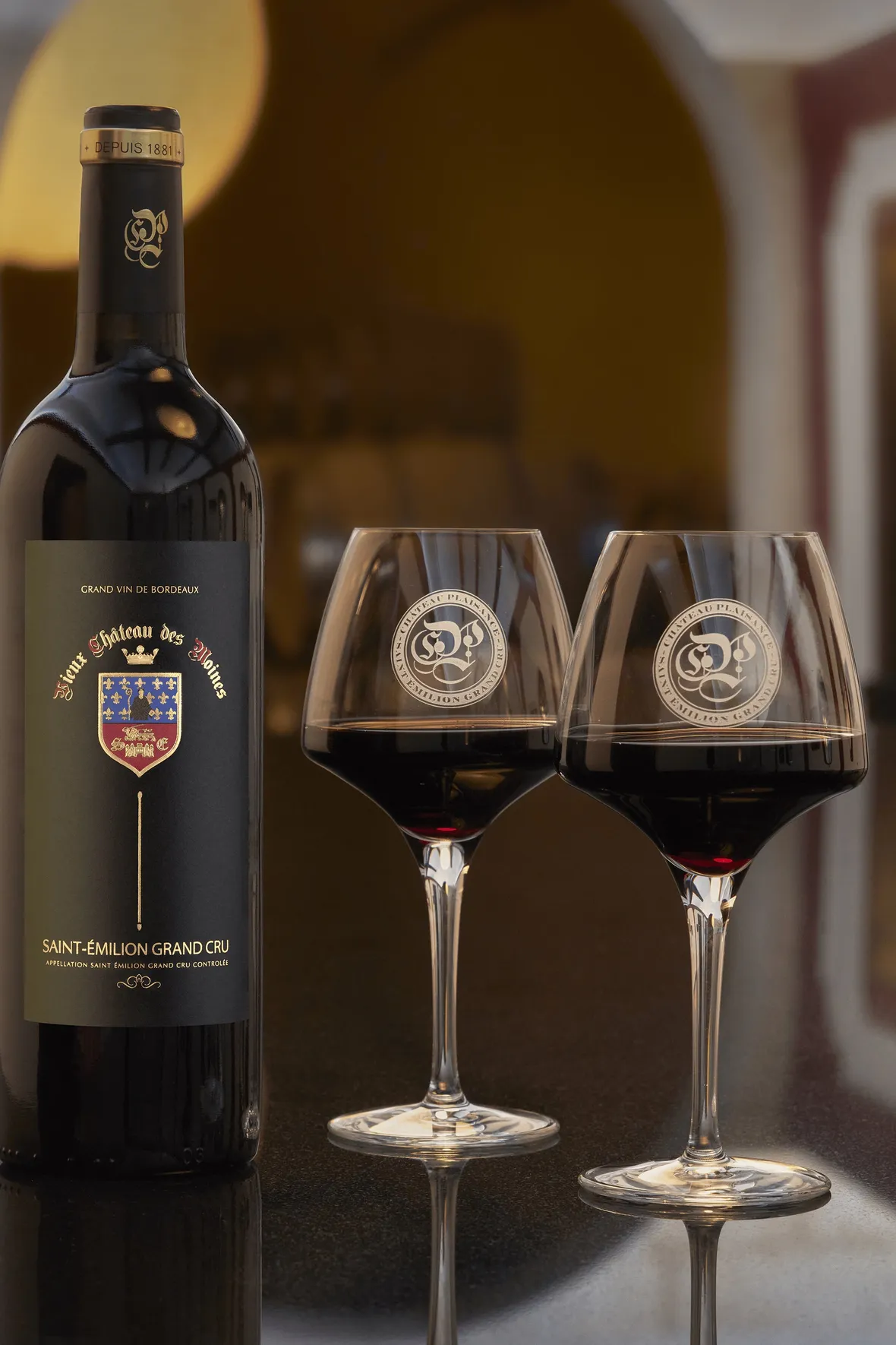 A bottle of Vieux Chateau des Moines Saint-Émilion Grand Cru red wine photographed with two glasses on the tasting table at Château Plaisance.