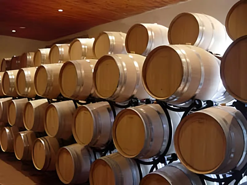 A large wine cellar with rows of oak barrels stacked high on racks, indicating the aging process of wine.