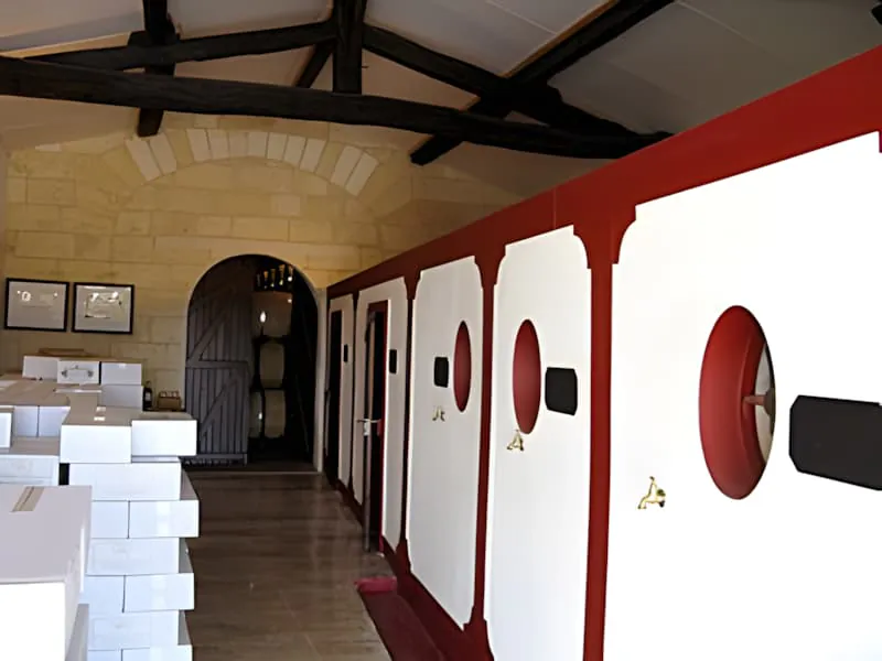 Interior of a wine sales room with white walls, red trim, exposed wooden beams, and framed certificates on the walls with a wooden entrance door.