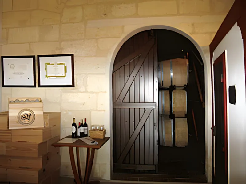 A closer view of the wine sales room entrance showing the distinctive wooden door, stone archway, and wine display table with certificates mounted on the wall.