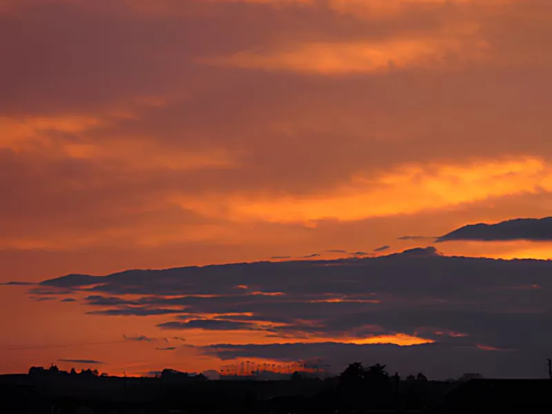 Un coucher de soleil dramatique avec des nuages orange et rouge vibrants s'étendant à travers le ciel au-dessus d'un paysage silhouetté.