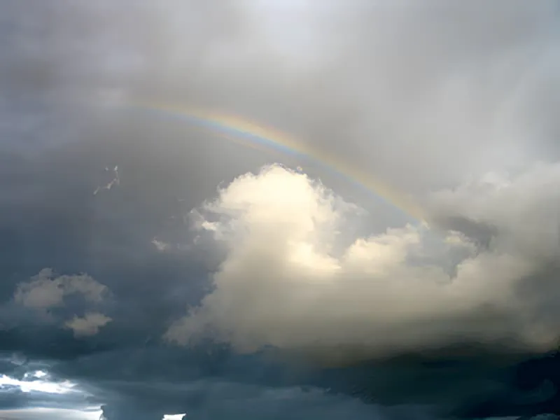 A partial rainbow arcing through gray storm clouds above the countryside landscape.