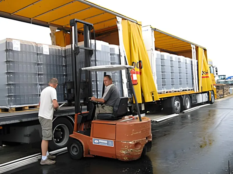 Industrial bottling equipment with a forklift operator and stacked metal bottle crates in a warehouse setting.
